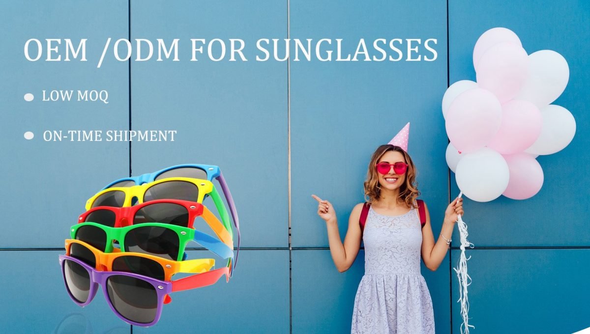 Happy attractive woman in sunglasses and party hat, holds air balloons, pointing finger on blue wall, showing copy space, outdoors. Dressed in tender dress.